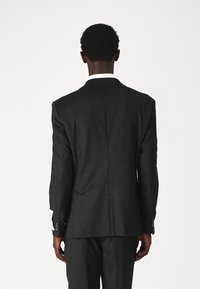 Veste de costume à carreaux sombres avec revers cranté, fente simple et poignets intérieurs clairs. Texture lisse et coupe structurée.