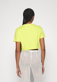 Kortärmad, cropped t-shirt i klargul bomull, kombinerad med vita byxor i strukturerad spets med detaljerade mönster.