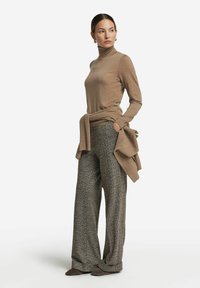 Beige Rollkragenpullover kombiniert mit weit geschnittenen, strukturierten Hosen im Fischgrätmuster, akzentuiert mit einem gestrickten Wickel um die Taille.