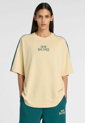 Donna che indossa una T-shirt oversize beige New Balance con strisce verde scuro sulle maniche e pantaloncini New Balance abbinati verde scuro.