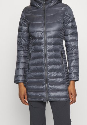 Femme portant une longue doudoune matelassée gris foncé avec fermeture éclair avant et poches latérales zippées, associée à un pantalon foncé.