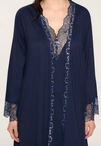 Granatowy szlafrok z długimi rękawami i koronkowym wykończeniem wzdłuż dekoltu i rękawów, prezentujący delikatny wzór kwiatowy. Wykonany z miękkiego materiału.