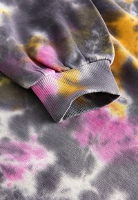 Felpa grigia con un motivo tie-dye, caratterizzata da accenti rosa, giallo e viola. Maniche a portafoglio e un tessuto morbido e strutturato.