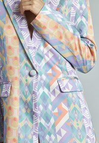 Blazer estampado en colores pastel, con formas geométricas, cuello muesca, dos bolsillos frontales y cierre de un solo botón.