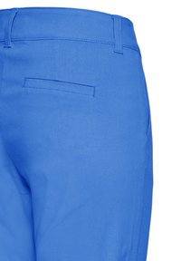 Jasnoniebieskie spodnie pokazujące tylną kieszeń, szlufki na pasek oraz boczny szew na białym tle.