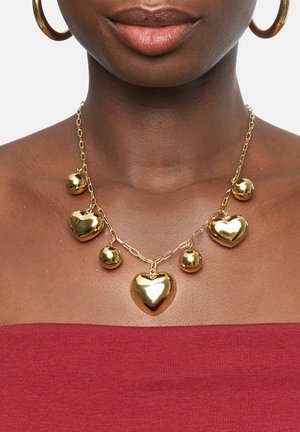 Collier doré avec des pendentifs en forme de cœur et ronds, doté d'un design en chaîne liée. Surface lisse et brillante avec une texture réfléchissante.