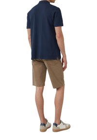 Granatowa koszulka polo, brązowe szorty i białe sneakersy z granatowymi akcentami. Luźny krój, krótkie rękawy i boczne rozcięcia w koszulce polo.