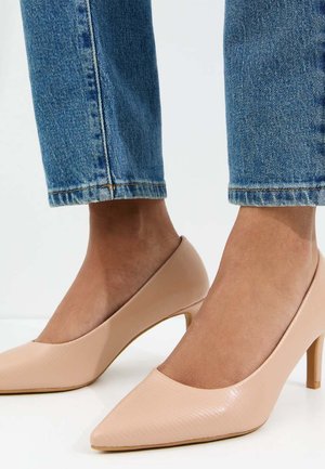 Piedi con indosso décolleté color nudo con punta a punta abbinati a jeans cropped in denim blu su sfondo semplice.