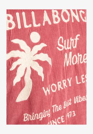 Tejido de pana rosa con texto blanco bordado y un diseño de palmera. Las frases clave incluyen "Surf More" (Surfea más) y "Worry Less" (Preocúpate menos), con una superficie texturada.