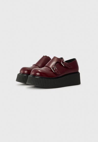 Scarpe da platform in pelle bordeaux con punta arrotondata, design a doppia fascia e suola nera testurizzata. Presentano dettagli in metallo.