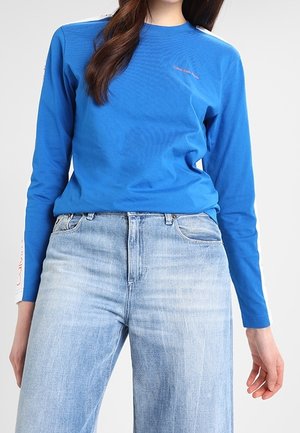 Blaues Langarmshirt mit Rundhalsausschnitt, verfügt über weiße Akzentstreifen auf den Schultern und das Calvin Klein-Logo in Pink auf der Brust.
