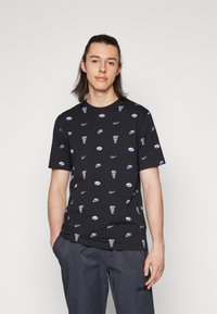 Camiseta de algodón negra con un patrón repetido de logotipos de Nike en blanco y morado y la frase "JUST DO IT". Diseño de cuello redondo.