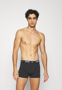Fekete pamut boxer alsónadrág fehér Nike logóval az elasztikus derékpánton, szoros illeszkedéssel és sima textúrával. A modell állva pózol.