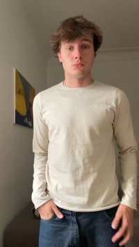 Camisa de manga larga color beige claro con cuello redondo, hecha de una tela suave, combinada con jeans de color azul oscuro. Manos en los bolsillos, fondo neutro.