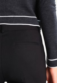 Pantalons noirs avec une coupe ajustée et une poche arrière. Le haut est en tissu tricoté gris avec des finitions blanches autour de l'ourlet et des manches.