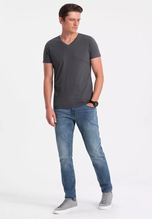 Grau V-Ausschnitt T-Shirt, kurze Ärmel, getragen mit hellblauen Jeans und grauen Sneakern. Einfaches Design, lässige Passform und sichtbare Stofftextur.