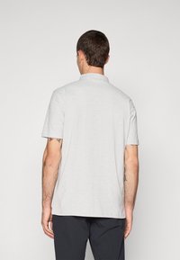 Grå polo skjorte laget av mykt stoff med krage og korte ermer. Har en rett nederkant og minimal detaljering.