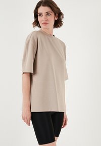 Beige oversized t-shirt med korte ærmer, glat tekstur, rund halsudskæring, parret med sorte tætsiddende cykelshorts.