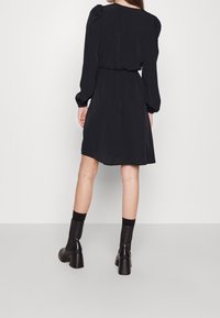 Mustalainen mekko, jossa on pitkät puff-hihat, elastinen vyötärö ja rento leikkaus. Yhdistetty mustien nilkkasaappaiden ja siihen sopivien sukkien kanssa.