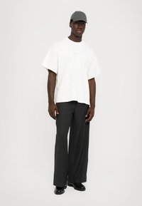 T-shirt bianca oversize con un logo sottile, abbinata a pantaloni grigi a gamba larga e scarpe nere. Completa il look con un cappello grigio.