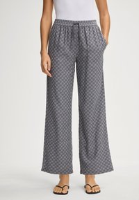 Šedé vzorované široké kalhoty s elastickým pasem a kapsami; látka má geometrický design. V kombinaci s černými žabkami.