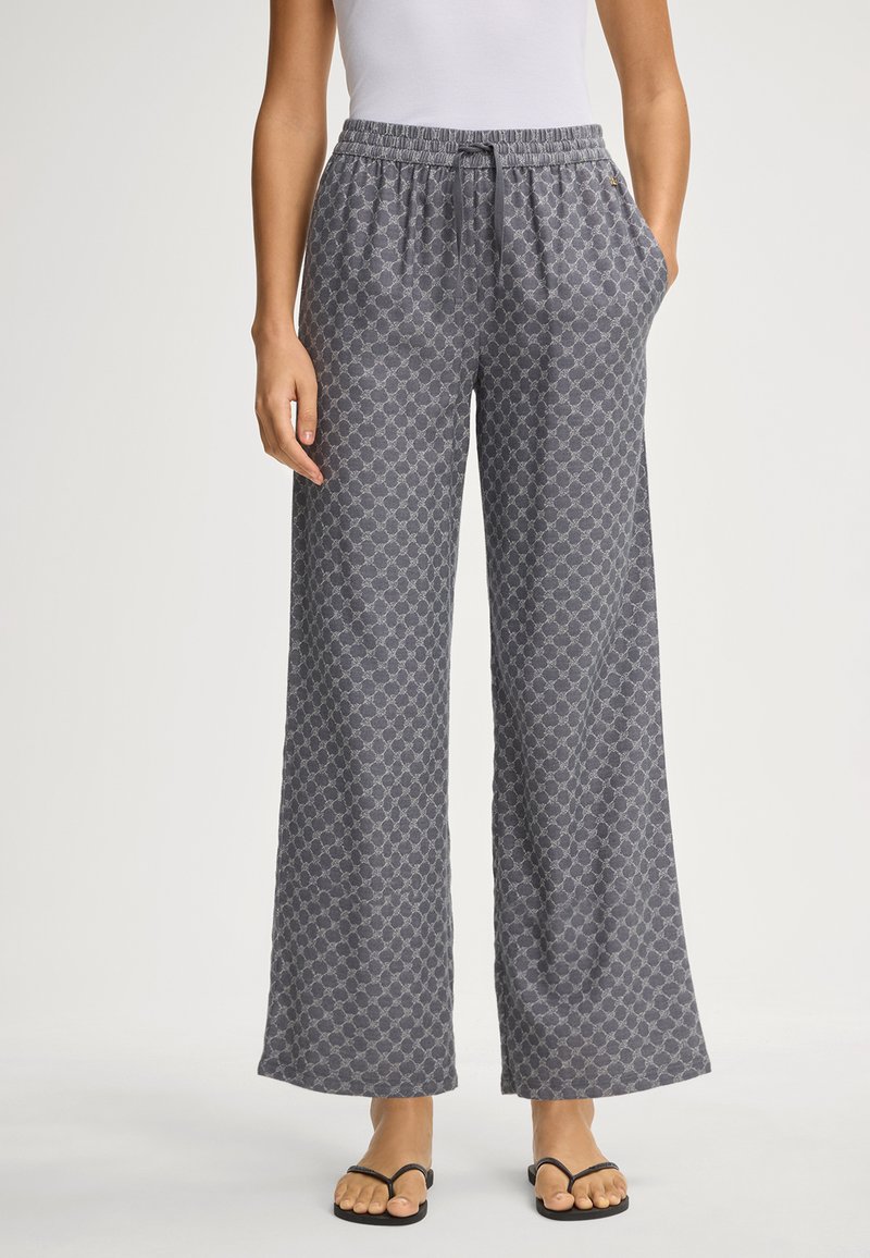 Šedé vzorované široké kalhoty s elastickým pasem a kapsami; látka má geometrický design. V kombinaci s černými žabkami.