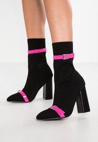 Mustat nilkkurit, joissa on vaaleanpunainen kiiltoinen hihna ja solki, teräväkärkiset ja joissa on teksturoitu paksu korko.