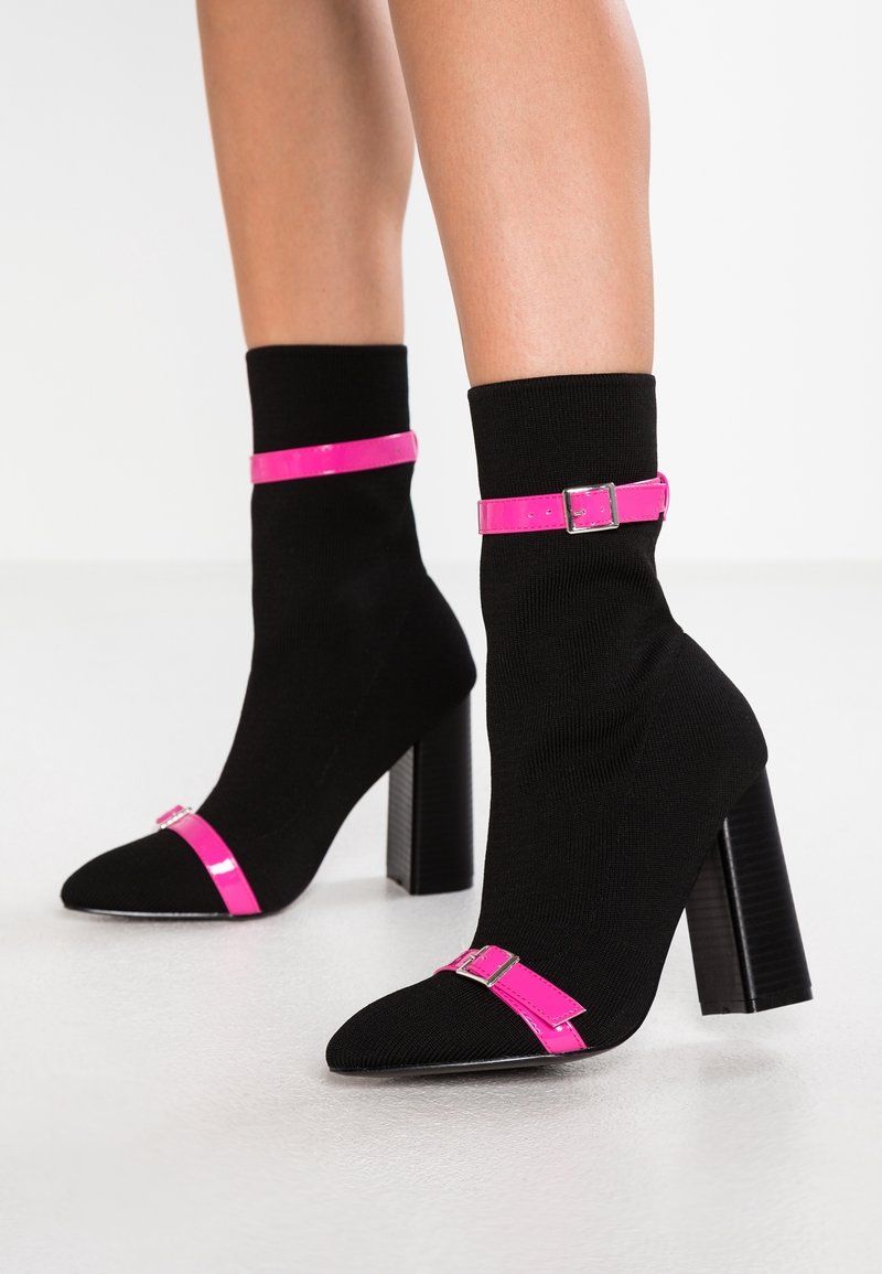 Mustat nilkkurit, joissa on vaaleanpunainen kiiltoinen hihna ja solki, teräväkärkiset ja joissa on teksturoitu paksu korko.