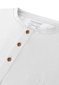 Das weiße Baumwollhemd hat einen Rundhalsausschnitt, fünf braune Knöpfe auf der Vorderseite und eine dezente Textur mit einem gestickten Logodetail.