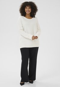 Cream-colored knit sweater with a scoop neckline and long sleeves, paired with black wide-leg pants and pointed black shoes.