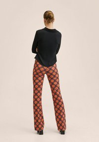Blouse noire à col, associée à un pantalon évasé à motifs dans un vibrant design floral rose, orange et noir. Des talons noirs imposants complètent le look.