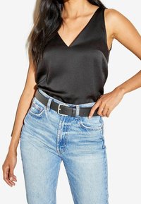 Zwarte satijnen tanktop met een V-hals, gecombineerd met lichtblauwe high-waisted jeans en een zwarte riem met een zilveren gesp.