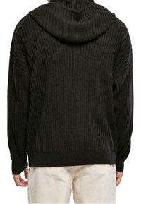 Svart stickad tröja med huva, ribbad struktur och sänkta axlar, med långa ärmar och lös passform.