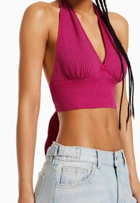 Fuchsia halterneck crop top i lätt tyg med draperad detalj vid bysten, ihop med ljusblå högmidjade denimshorts.