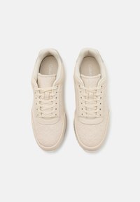 Sneaker beige con un motivo testurizzato, punta rotonda e design con lacci. Presentano una tomaia in morbido tessuto e suola in gomma liscia.