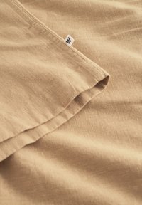 Tissu beige avec une finition texturée, comportant un ourlet replié et une petite étiquette, mettant en valeur un matériau lisse et léger.