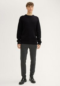Czarny sweter z prążkowanego dzianiny z okrągłym dekoltem, w zestawieniu z ciemnoszarymi zwężającymi się spodniami i czarnymi sznurowanymi butami. Minimalistyczny design.