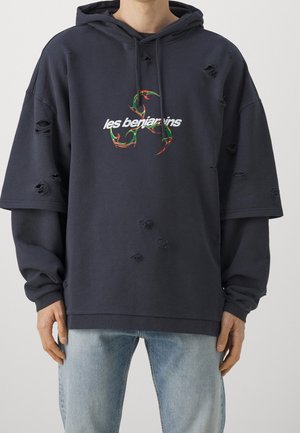 Sudadera de gran tamaño en color marino con detalles desgastados, que presenta un colorido texto gráfico "les benjamins" en la parte frontal y una textura de algodón suave.