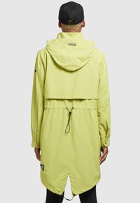 Ljusgrön regnjacka med huv, åtsittande midja, tryckknappar och rundad fåll. Har dragsko-detaljer och logopatch.