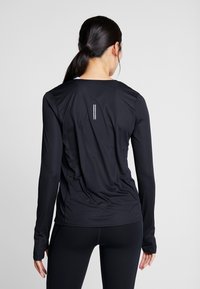 Musta pitkähihaine urheilupaita, jossa on pyöreä kaula-aukko, sileä rakenne ja heijastavat kaksoisraidat takana, suunniteltu aktiiviseen käyttöön.