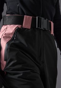 Black and pink ski pants featuring a wide black belt, zippered pockets, smooth texture, and contrasting side panels for added detail.