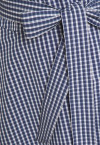 Blå och vit rutigt tyg har vertikala och horisontella ränder med en knytbåge i midjan. Texturen verkar slät och vävd.