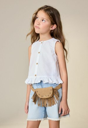 Noor tüdruk, kes kannab valget varrukateta nööpidega toppi ja teksaseid lühikesi pükse, aksessuaariks pruun tuttidega vöökott, vaadates ülespoole.