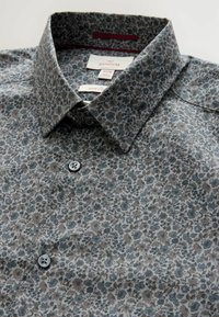 Blumenhemd in Grau, aus weichem Stoff mit einem kleinen Blumenmuster, einem spitzen Kragen und grauen Knöpfen auf der Vorderseite.