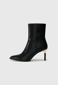 Stivale alla caviglia in pelle nera con punta appuntita e tacco accentato in oro contrastante. Texture liscia, design elegante e silhouette aderente.