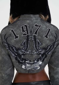 Cropped gray suede jacket featuring black eagle embroidery, the year "1971," and a white ribbon with "Ed Hardy" text.