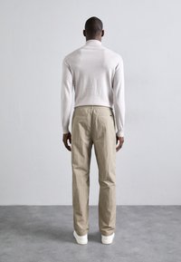 Light beige trousers with a textured fabric and elastic waistband, paired with a cream fitted long-sleeve top, viewed from the back.