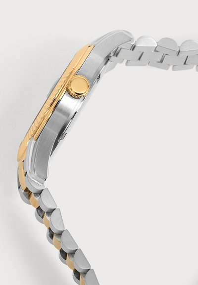 Montre-bracelet fine vue de côté montrant un boîtier métallique argent et or avec une couronne dorée et un bracelet bicolore argent et or relié.
