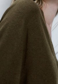 Olijfgroene, gestructureerde wollen trui met een losse pasvorm en brede mouwen, voorzien van een diepe V-hals en een zachte, licht fluweelachtige oppervlakte.