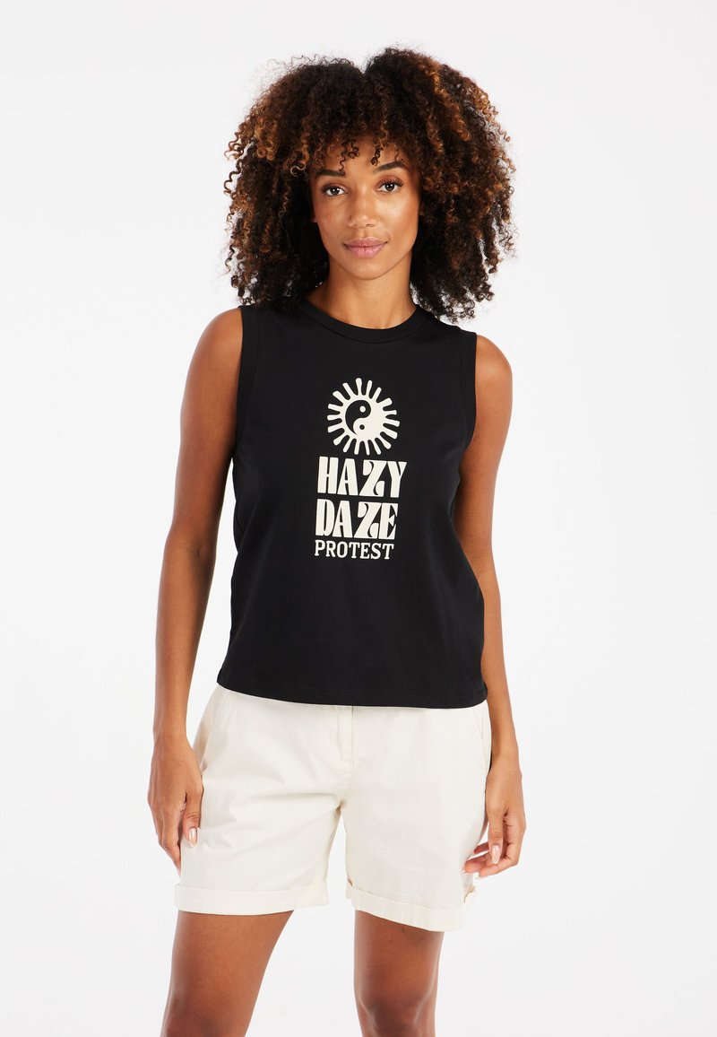 Top negro sin mangas con un atrevido estampado gráfico blanco que dice "HAZY DAZE PROTEST" y un diseño de sol, combinado con pantalones cortos de color claro.